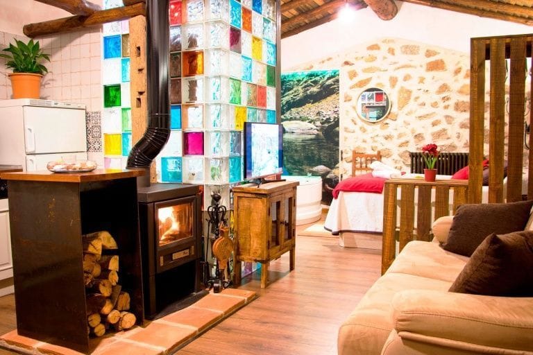 Casa Rural El Cuco: estancia con estufa de leña y cama al fondo